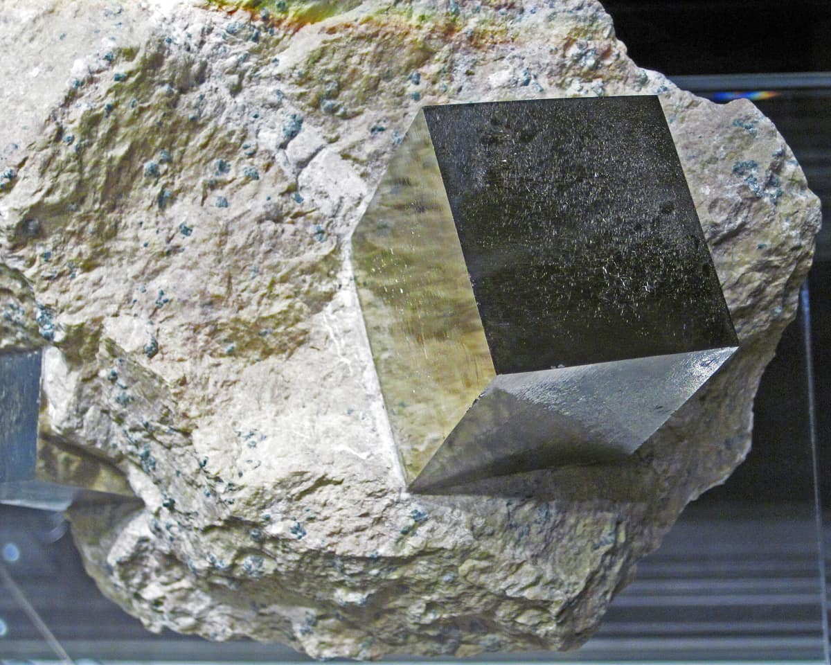 Un cube de pyrite doré aux arêtes vives, encastré dans une marne claire.